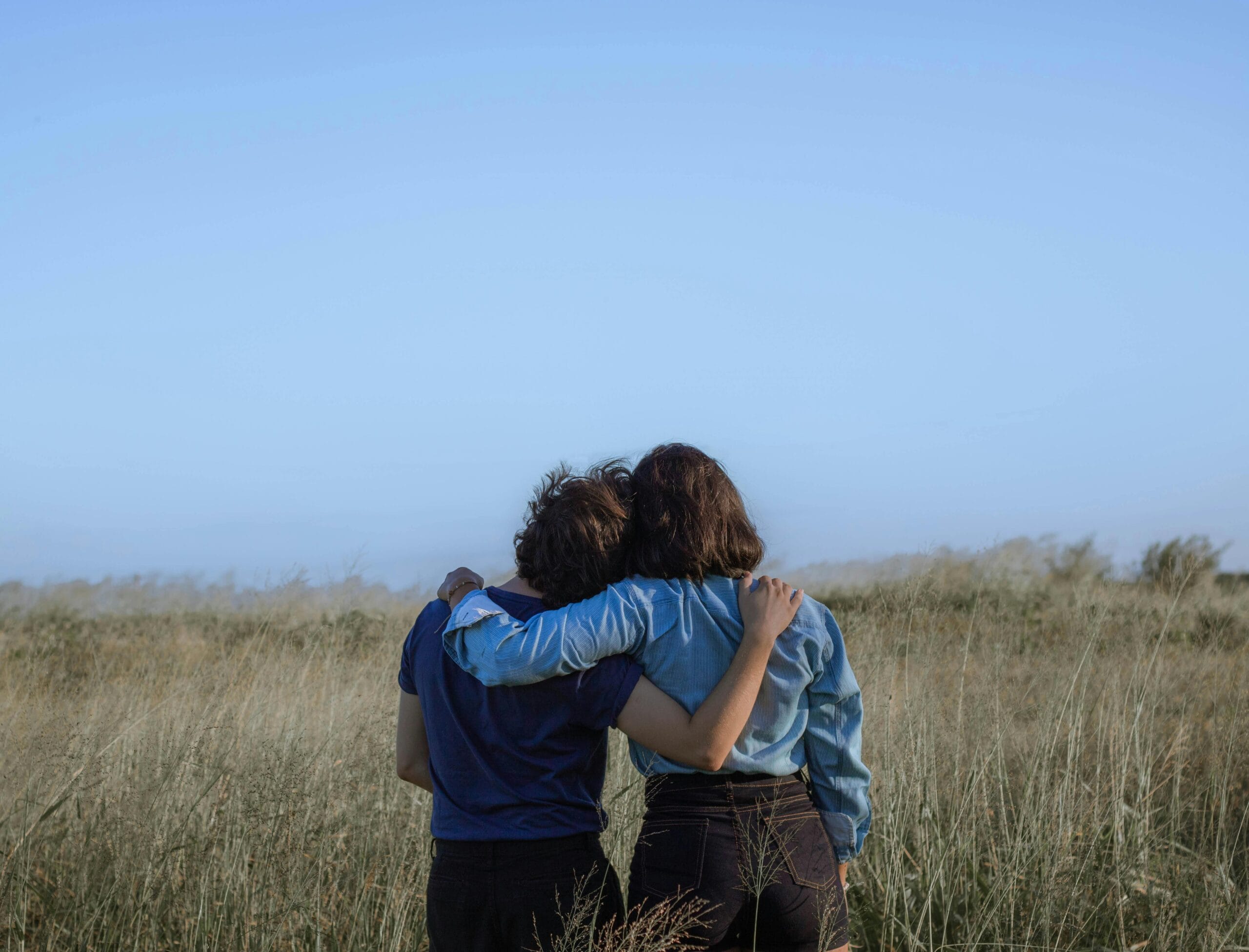 Holistic Mind & Body Wellness - Find A Therapist Back view unrecognizable girlfriends wearing casual clothes hugging each other while standing on grassy vast field in summer countryside